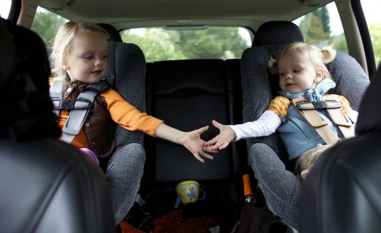 Caucasian sisters holding hands in back seat of car