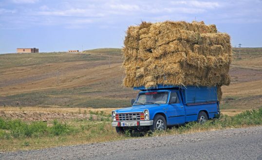 Blue pickup truck heavily loaded with hay bales in rural Iran